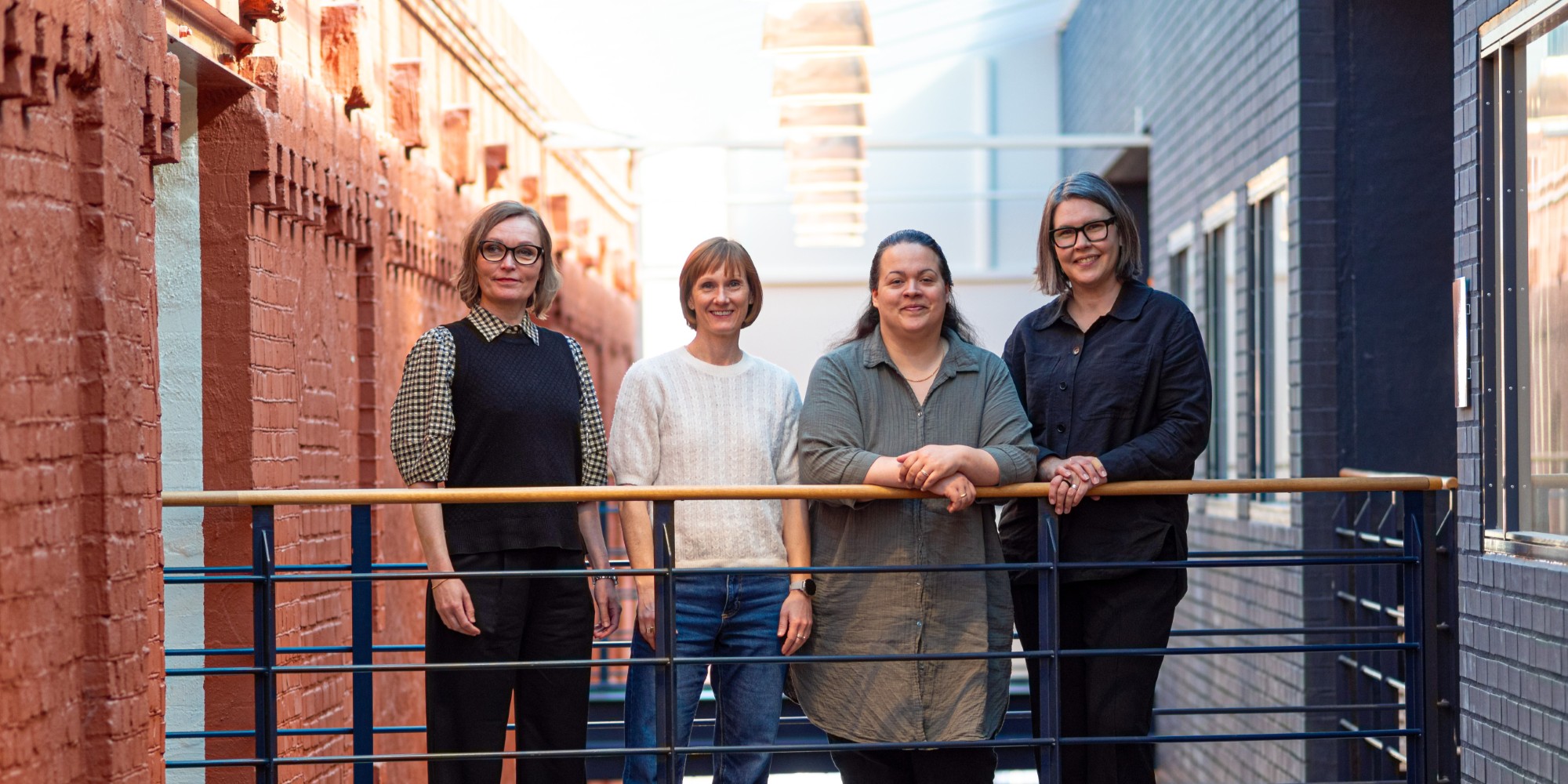 Fyra personer som står vid ett räcke med ett glastak som släpper igenom solljuset uppifrån.