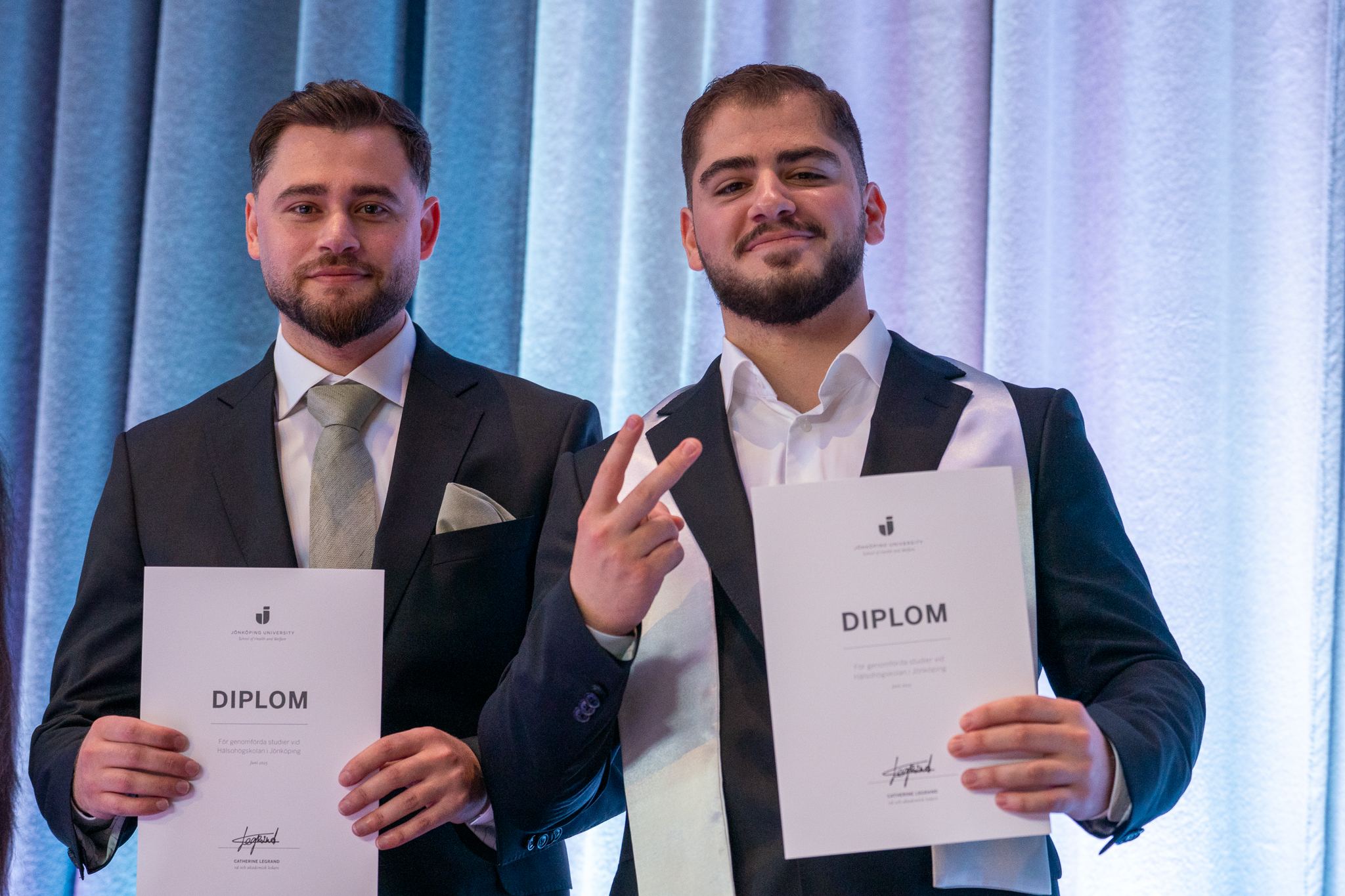 Två killar som håller i sina examensdiplom och tittar in i kameran.